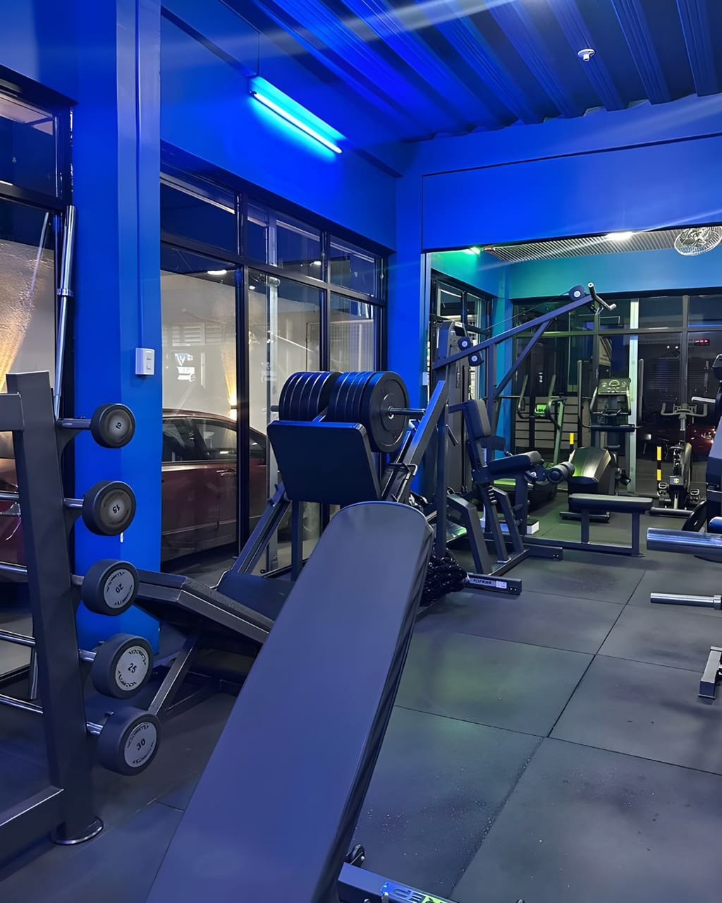 San Miguel branch floor in blue light, with a bench, a dumbbell rack, a leg press and floor-to-ceiling windows